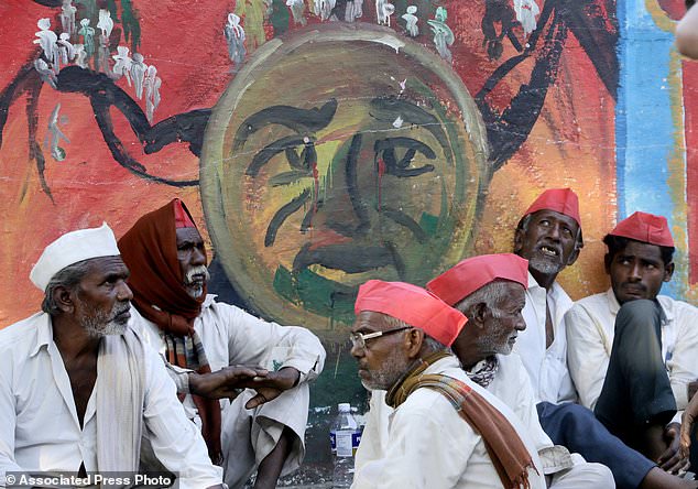 Indian farmers sit in front of a graffiti at the end of their six day long march on foot, in Mumbai, India, Monday, March 12, 2018. Tens of thousands of farmers from across western India have arrived in Mumbai demanding, among other things, a waiver of farm loans and fair prices for their produce as India's agriculture sector struggles amid years of declining earnings. The farmers reached India's business capital Monday after marching on foot for up to six days and plan to surround the state legislature of the western state of Maharashtra in Mumbai. (AP Photo/Rajanish Kakade)